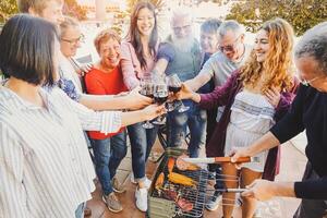 Lycklig familj glädjande och toasting med röd vin glas på utegrill fest - människor med annorlunda åldrar har roligt dricka och grillning kött på bbq middag - vänskap, mat och helgen aktiviteter foto