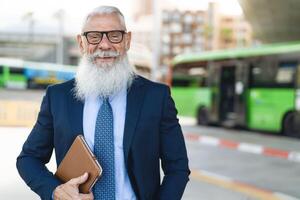 Lycklig senior företag man skrattande på buss station innan gående till arbete foto