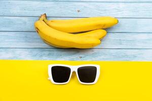 gul bananer och solglasögon lögn på en blå trä- bakgrund och en gul bakgrund foto
