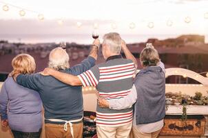 Lycklig seniors har roligt på taket utegrill fest - äldre familj dining och glädjande med röd vin glasögon på bbq på terrass - människor livsstil mat och dryck begrepp foto