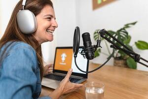 mogna kvinna inspelning en podcast använder sig av mikrofon och bärbar dator från henne Hem studio foto