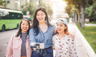 Lycklig asiatisk vänner vlogging i stad buss station - trendig ung människor använder sig av gimbal smartphone utomhus- - vänskap, teknologi, ungdom livsstil och social media begrepp foto
