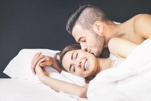 Lycklig par vakna upp i de morgon- på Hem - ung älskare har en anbud ögonblick pojkvän kissing hans flickvän i säng - kärlek och lycka begrepp foto