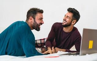 Lycklig Gay män par använder sig av bärbar dator i säng - homosexuell kärlek och kön jämlikhet i relation begrepp foto