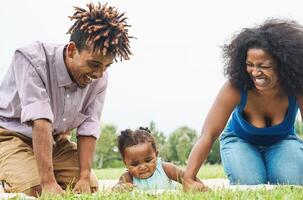 Lycklig afrikansk familj har roligt tillsammans i offentlig parkera - svart far och mor innehav hand med deras dotter - människor och förälder enhet begrepp foto