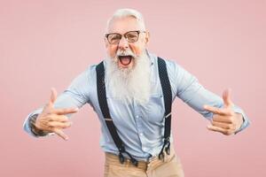 senior man har roligt Framställ i främre kamera - Lycklig mogna manlig njuter pensionerad tid - äldre människor livsstil och hipster kultur begrepp - rosa bakgrund foto