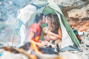 resa par kissing medan Sammanträde i de tält med deras sällskapsdjur - Lycklig man och woan har en romantisk ögonblick semester camping runt om sten berg Nästa till de brand - kärlek, resa, högtider begrepp foto