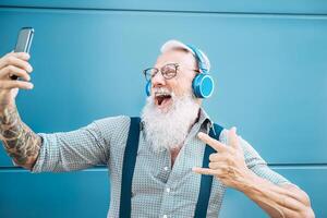 senior galen man tar själv video medan lyssnande musik med hörlurar - hipster kille har roligt använder sig av mobil smartphone Spellista appar - lycka, teknologi och äldre livsstil människor begrepp foto