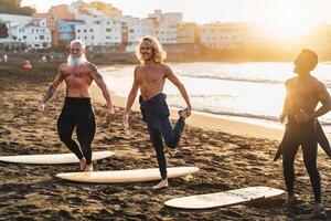 Lycklig passa surfare med annorlunda ålder och lopp håller på med värma upp övningar innan surfing under solnedgång tid. extrem sport livsstil och vänskap begrepp foto