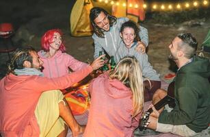 grupp av vänner har roligt glädjande med öl på de strand med tält på natt - Lycklig ung människor spelar gitarr och skrattande tillsammans - vänskap, semester och camping livsstil begrepp foto