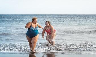 Lycklig plus storlek kvinnor har roligt på de strand under sommar semester - kurvig självsäker människor livsstil begrepp foto