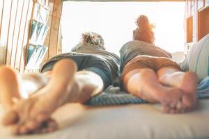 Lycklig par liggande på säng inuti minibuss ser på solnedgång - resa människor stunder under en väg resa - semester, kärlek och relation, ungdom livsstil begrepp foto