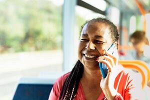 Lycklig afrikansk senior kvinna har en ring upp med smartphone medan reser förbi buss foto