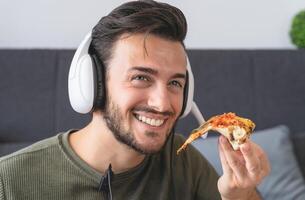 ung man äter leverans pizza på Hem - Lycklig kille har måltid medan video kallelse med familj i levande rum - snabb mat och ungdom människor underhållning begrepp foto