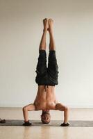en man med en naken torso gör yoga stående på hans huvud inomhus. kondition tränare foto