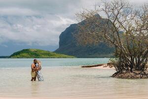 en flicka i en baddräkt och en man i shorts stå i de hav mot de bakgrund av montera le morne på de ö av mauritius.a par i de vatten se in i de distans av de hav foto