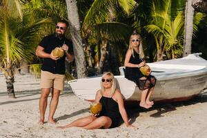 en eleganta familj i svart kläder med kokosnötter i deras händer på de strand av de ö av mauritius.vacker familj på de ö av mauritius i de indisk hav foto