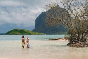 en flicka i en baddräkt och en man i shorts stå i de hav mot de bakgrund av montera le morne på de ö av mauritius.a par i de vatten se in i de distans av de hav foto
