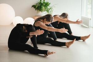 en grupp av flickor i svart håller på med yoga poser inomhus. kvinnor är engagerad i kondition foto