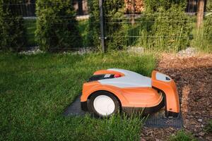 ett orange robot gräsmatta gräsklippare står på de bas och är laddad från elektricitet i de gård foto