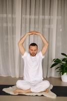 en man i vit sportkläder är håller på med yoga med en kondition rum. de begrepp av en friska livsstil foto