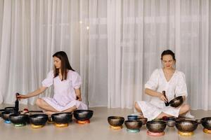 två kvinna yoga lärare spela på tibetan skålar i de Gym under en yoga reträtt foto