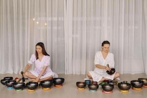 två kvinna yoga lärare spela på tibetan skålar i de Gym under en yoga reträtt foto