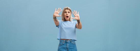 kvinna livrädd skrikande och be sluta. porträtt av chockade panik bekymrad blond kvinna i denim shorts och tillfällig t-shirt dragande händer i Nej gest dropp käke och rynkar foto