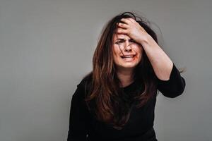 en misshandlade kvinna i svart kläder på ett isolerat grå bakgrund. våld mot kvinnor foto
