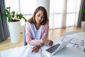 ung kvinna arbetssätt bärbar dator. företag kvinna upptagen arbetssätt på bärbar dator dator på kontor. affärskvinna Sammanträde på ljus modern arbete station och skriver på bärbar dator foto