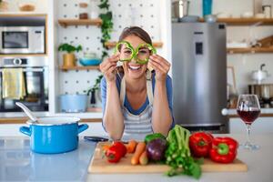 Foto av ung kvinna leende med grön peppar skivor medan matlagning sallad med färsk grönsaker i kök interiör på Hem