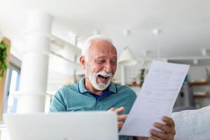 överraskad skrattande Lycklig gammal mogna pensionerad man ser genom papper dokumentera, känsla upphetsad analyserar finansiell information, få skatter återbetalning eller Bank lån godkännande på Hem. foto