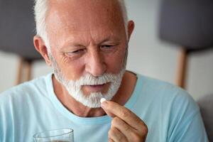 senior man tar piller med glas av vatten i hand. betonade mogna man dricka nersövd antidepressivt medel medicin. man känner deprimerad, tar läkemedel. mediciner på arbete foto