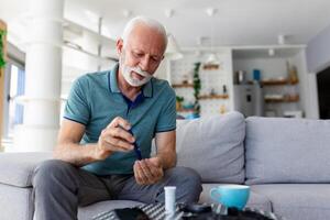 mogna man testning för hög blod socker. man innehav enhet för mätning blod socker, håller på med blod socker testa. senior man kontroll blod socker nivå förbi glukometer och testa rand på Hem foto