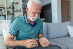 senior man tar piller med glas av vatten i hand. betonade mogna man dricka nersövd antidepressivt medel medicin. man känner deprimerad, tar läkemedel. mediciner på arbete foto