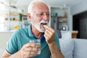 senior man tar piller med glas av vatten i hand. betonade mogna man dricka nersövd antidepressivt medel medicin. man känner deprimerad, tar läkemedel. mediciner på arbete foto