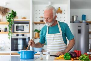 Lycklig senior man har roligt matlagning på Hem - äldre person framställning hälsa lunch i modern kök - pensionerad livsstil tid och mat näring begrepp foto