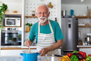 Lycklig senior man har roligt matlagning på Hem - äldre person framställning hälsa lunch i modern kök - pensionerad livsstil tid och mat näring begrepp foto