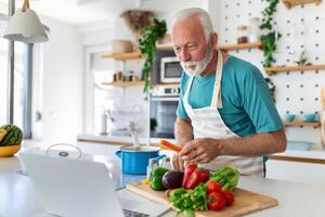 Lycklig senior man har roligt matlagning på Hem - äldre person framställning hälsa lunch i modern kök - pensionerad livsstil tid och mat näring begrepp foto