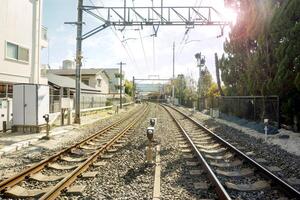 metall och stengods järnväg spår och stadsbild med Sol blossa och suddigt bakgrund av folkmassan människor väntar tåg på tåg plattform. foto