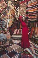 en skön flicka i en röd klänning i en traditionell turkiska interiör med många mattor på de vägg foto