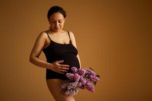studio porträtt av en skön gravid kvinna förväntar sig bebis, innehav mage, Framställ i svart underkläder isolerat på beige foto
