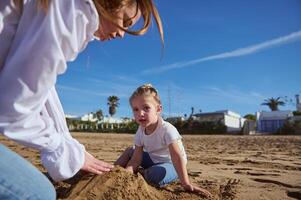 Lycklig av mor och dotter byggnad slott i sand på strand. familj livsstil, fritid aktivitet, människor. semester foto