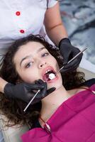 tandläkare granskning tänder av en ung kvinna patient i en dental klinik. tandvård begrepp. tandläkare och patient i de dental kontor. foto