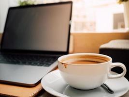 laptop och en kopp kaffe med morgonljus i caféet. foto