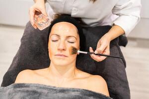 beskära kosmetolog applicering ansiktsbehandling gel på ansikte med borsta under hud behandling i skönhet Centrum. foto