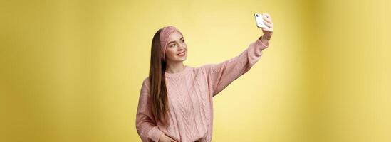 populär glamour ung kvinna internet livsstil bloggare tar selfie på ny smartphone förlängning ärm tar bild själv mot gul bakgrund leende på mobiltelefon skärm, Framställ fräck foto