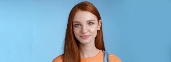 utgående ung rödhårig flicka blå ögon bär orange t-shirt overall leende angenämt vardagligt talande stående Bra humör glad känslor blå bakgrund, lyssnande intressant konversation foto