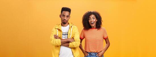 två afrikansk amerikan vänner stående över orange bakgrund, flicka tänker aning är grymt bra känsla upphetsad och glad medan pojkvän varelse missnöjd och likgiltig till föga imponerande planen foto