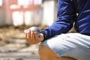 spelare håll en petanque boll i deras händer och förbereda till kasta den i beställa till plats de petanque boll som stänga till de mål boll som möjlig. foto